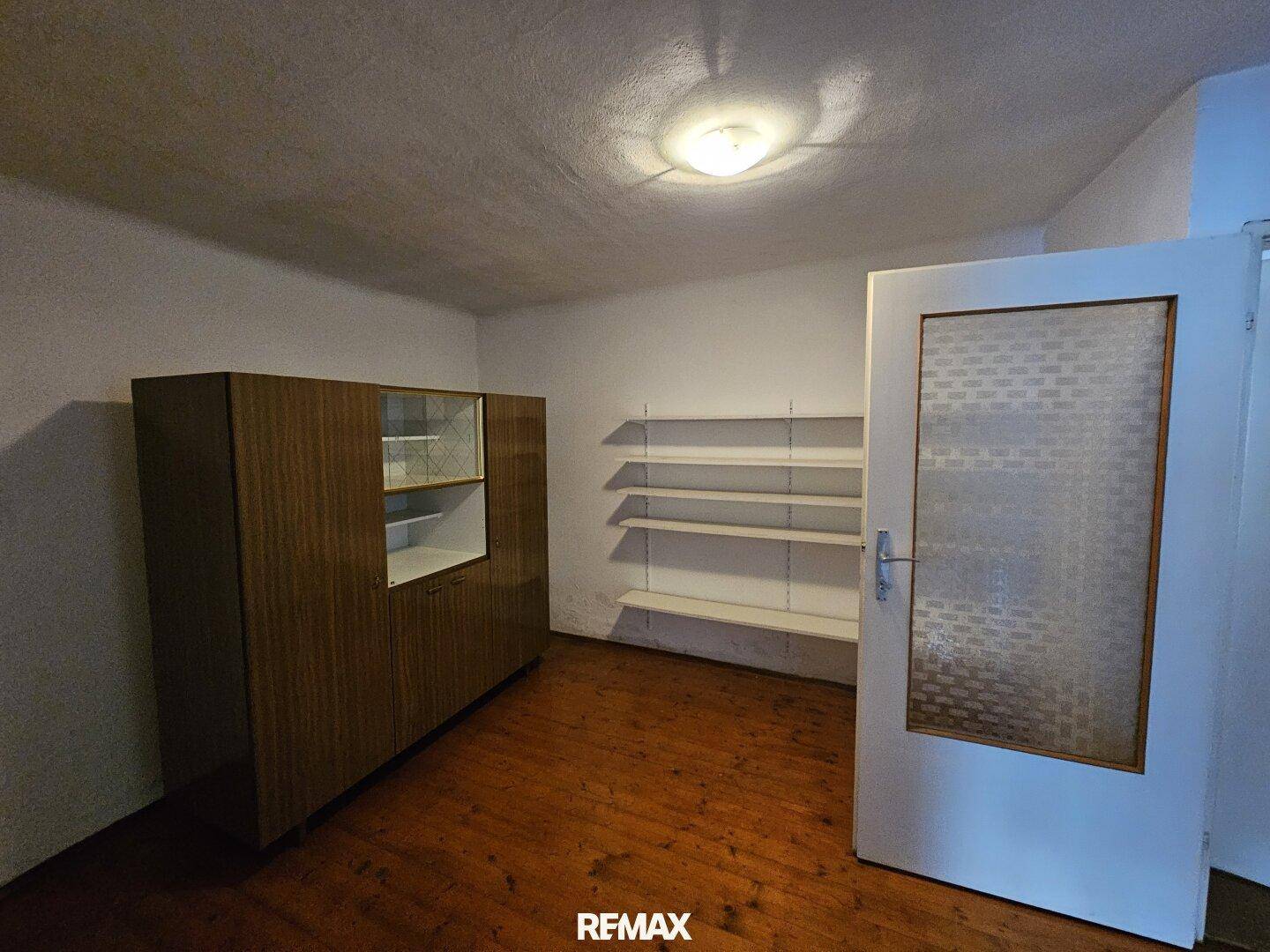 Kleiner Raum mit Holzboden, Regalen und einem Schrank.