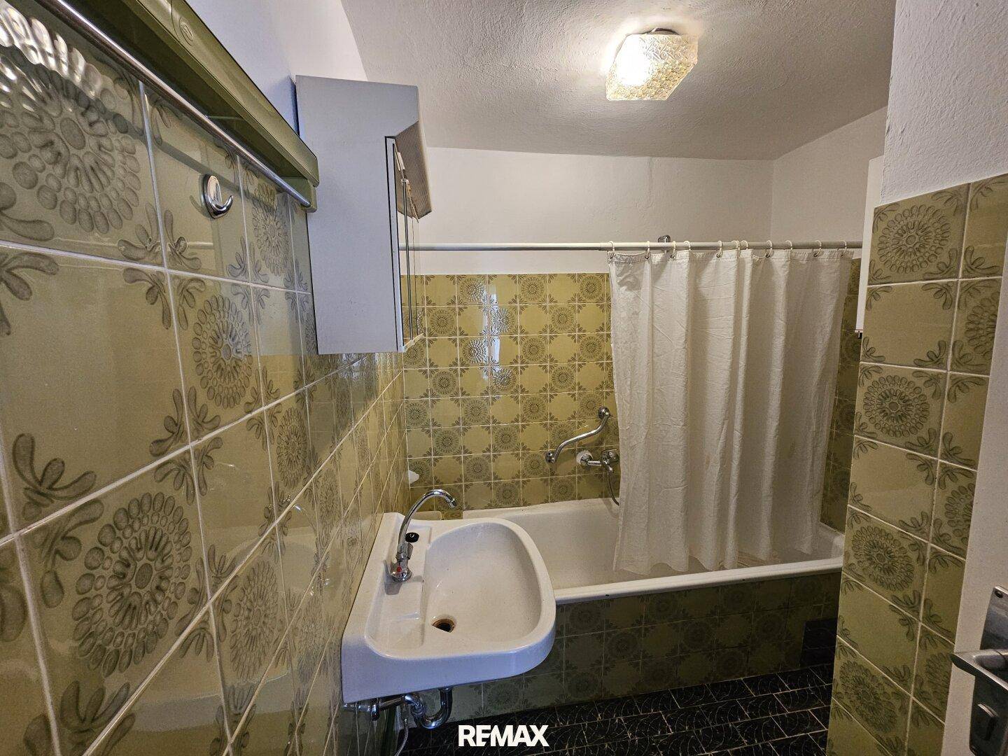 Badezimmer mit Badewanne, Waschbecken und gemusterten Fliesen im 80er-Jahre-Stil.