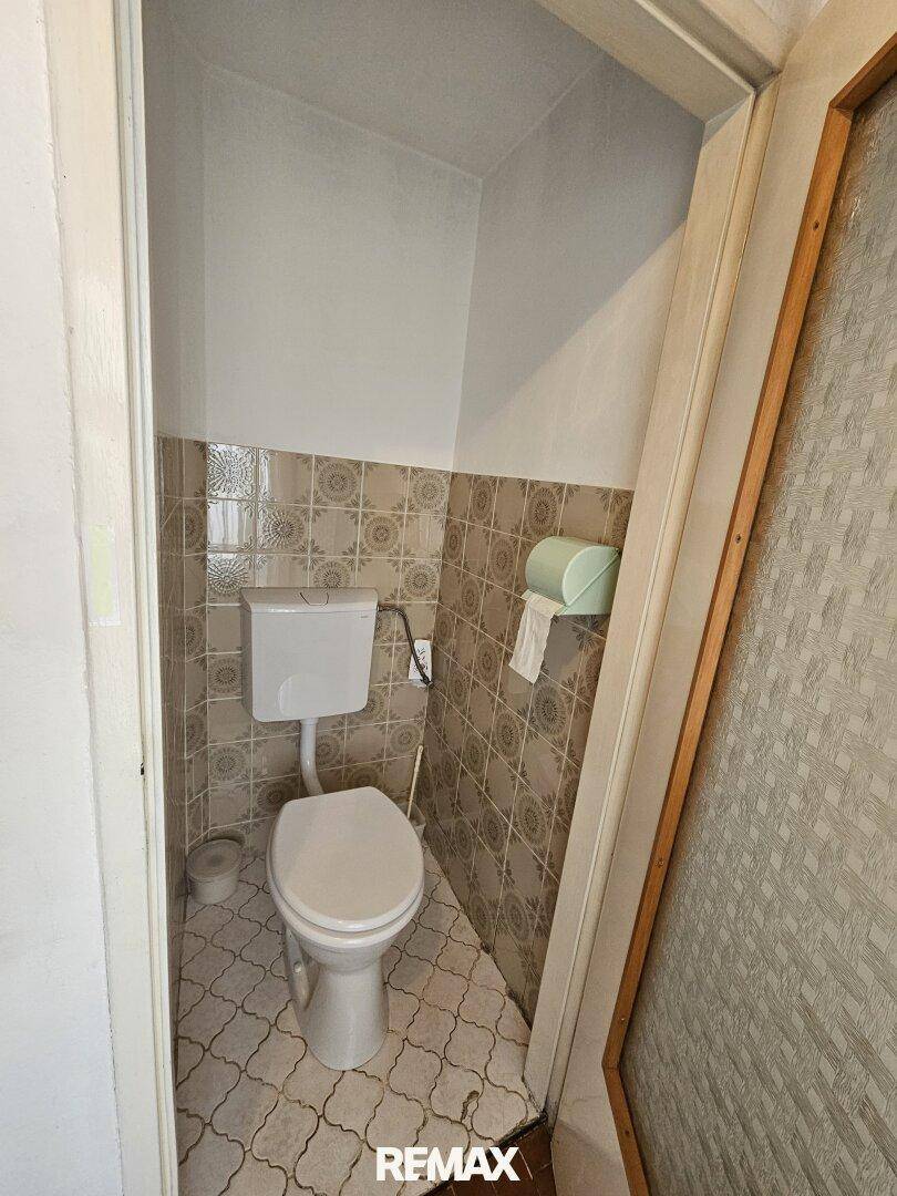 Separate Toilette mit WC und gemusterten Wand- und Bodenfliesen.