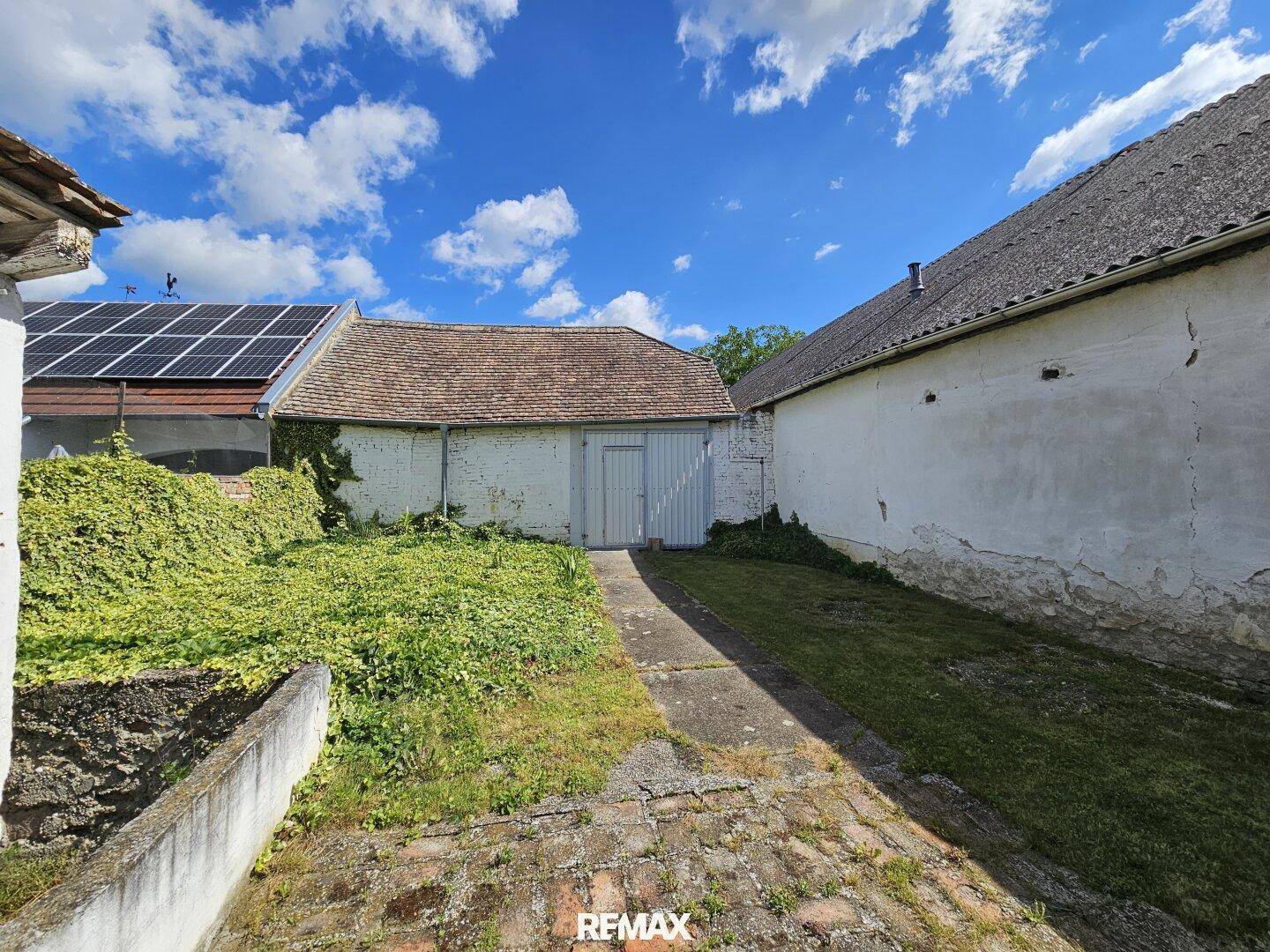 Hinterhof mit Gartenfläche, Nebengebäude und Photovoltaikanlage auf dem Dach.