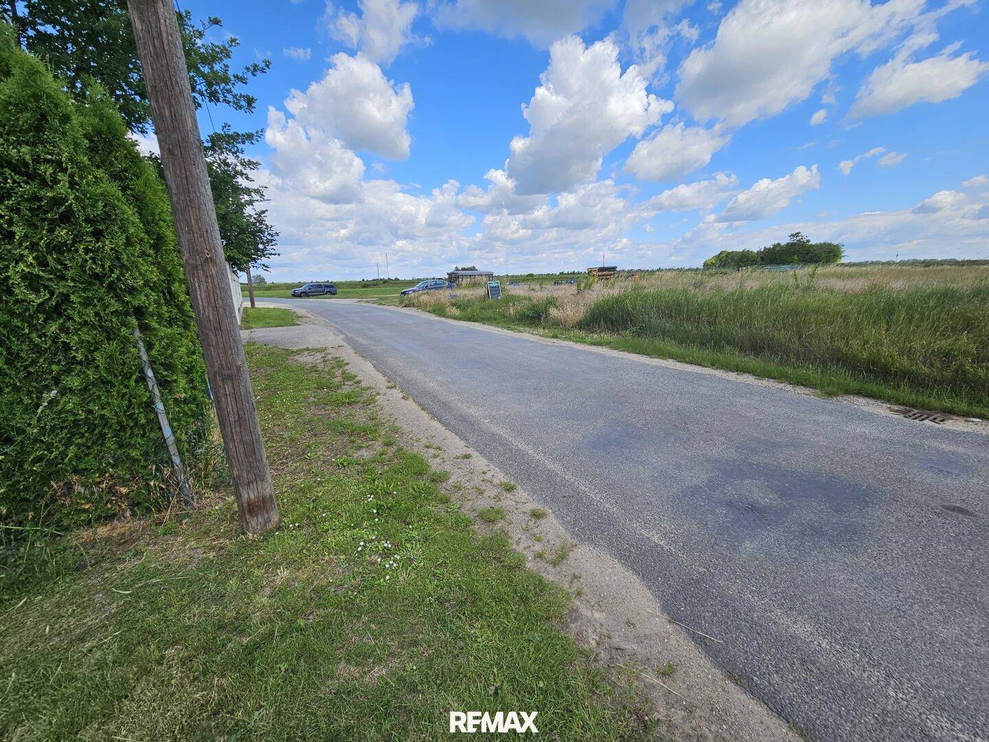 Ländliche Straße mit Feldern und weitem Himmel im Hintergrund.