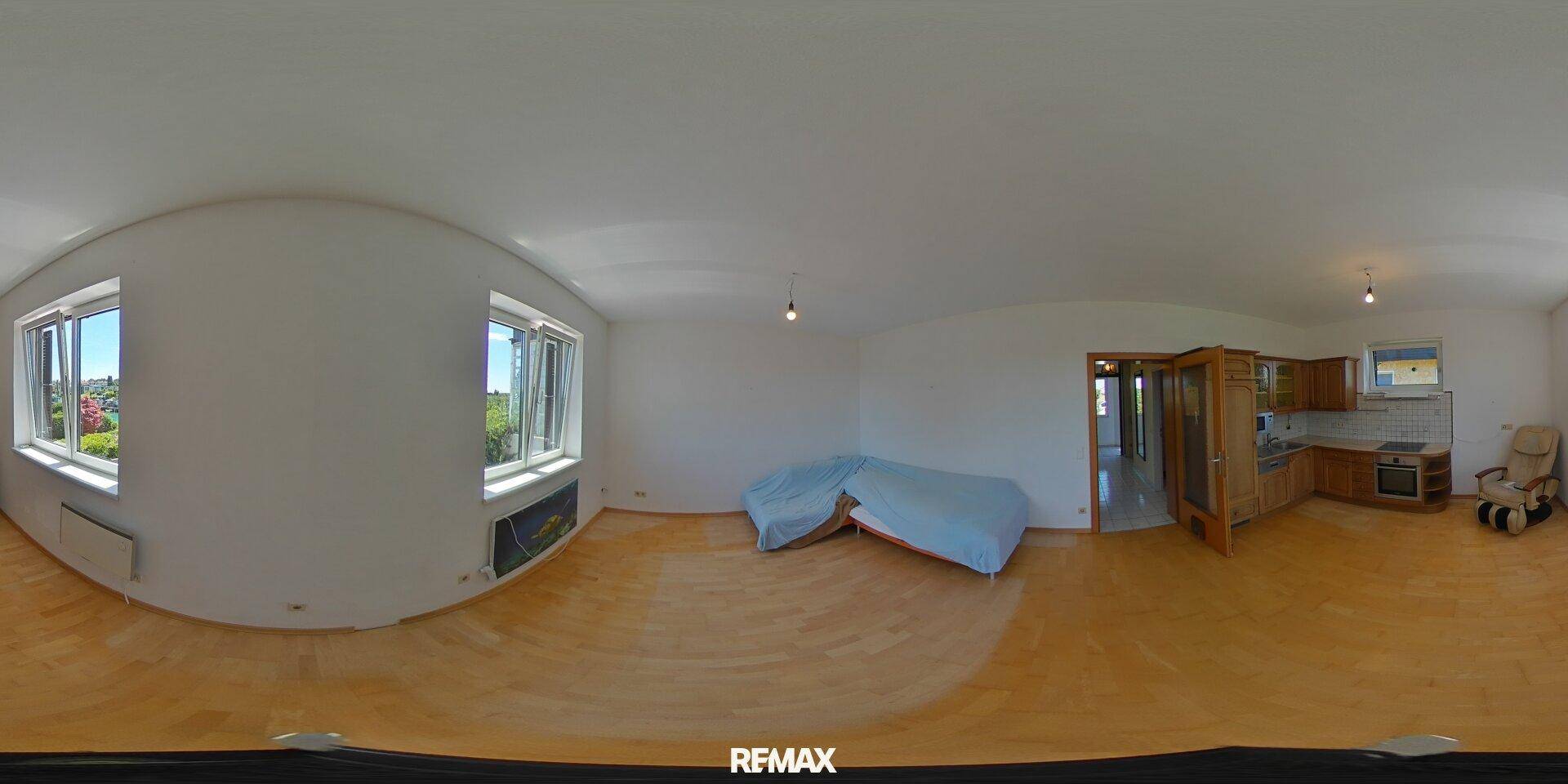 Geräumiger Wohn-Essbereich mit Holzboden und einer integrierten Küchenzeile im Hintergrund.