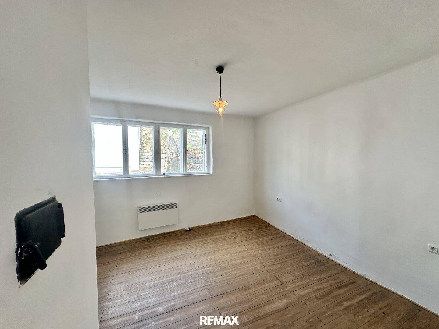 Leeres Schlafzimmer mit Holzdielenboden und einem Fenster, das den Blick nach draußen freigibt.
