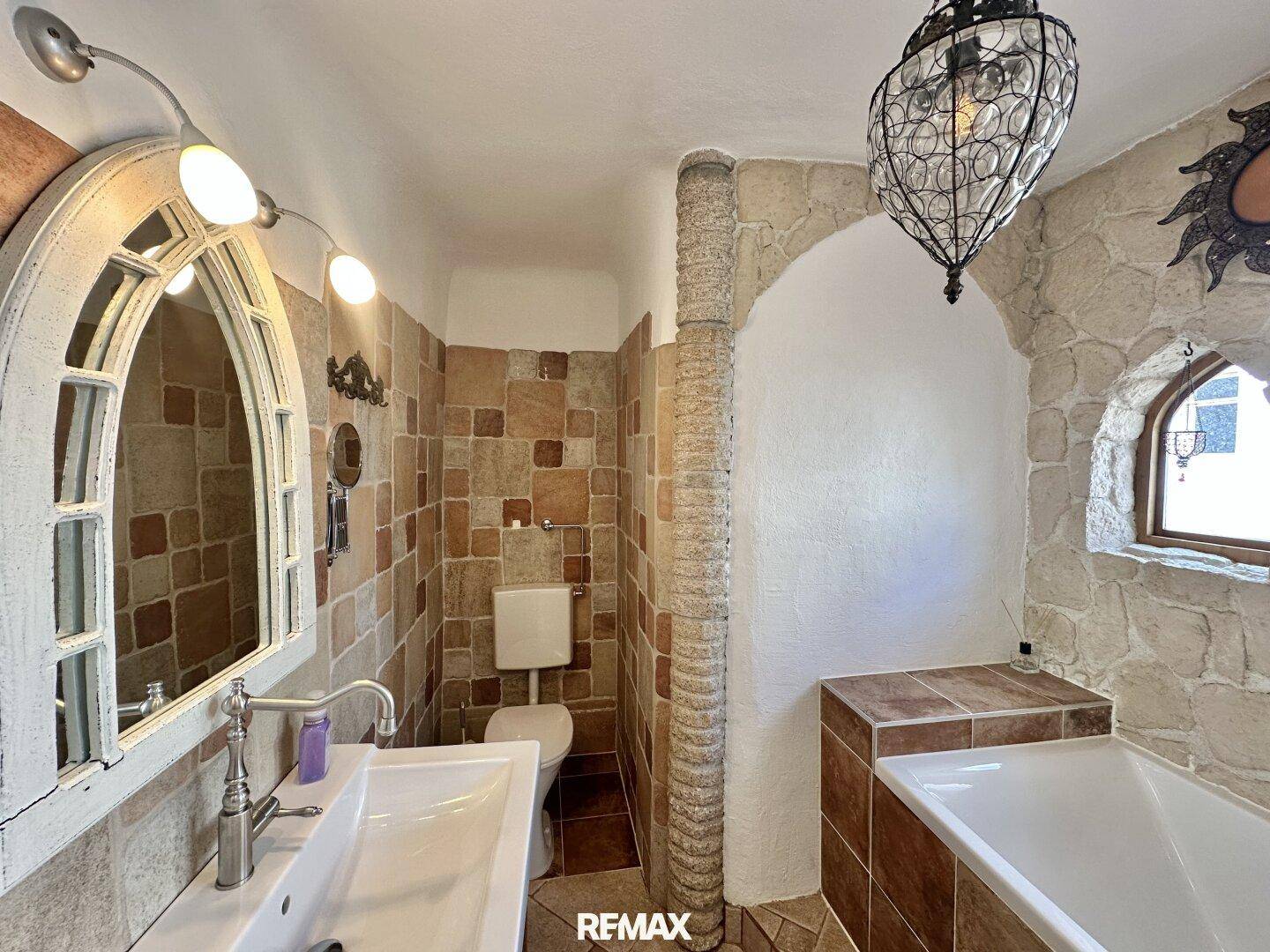 Rustikales Badezimmer mit Steinwänden, Fliesenboden und einer Badewanne im traditionellen Stil.