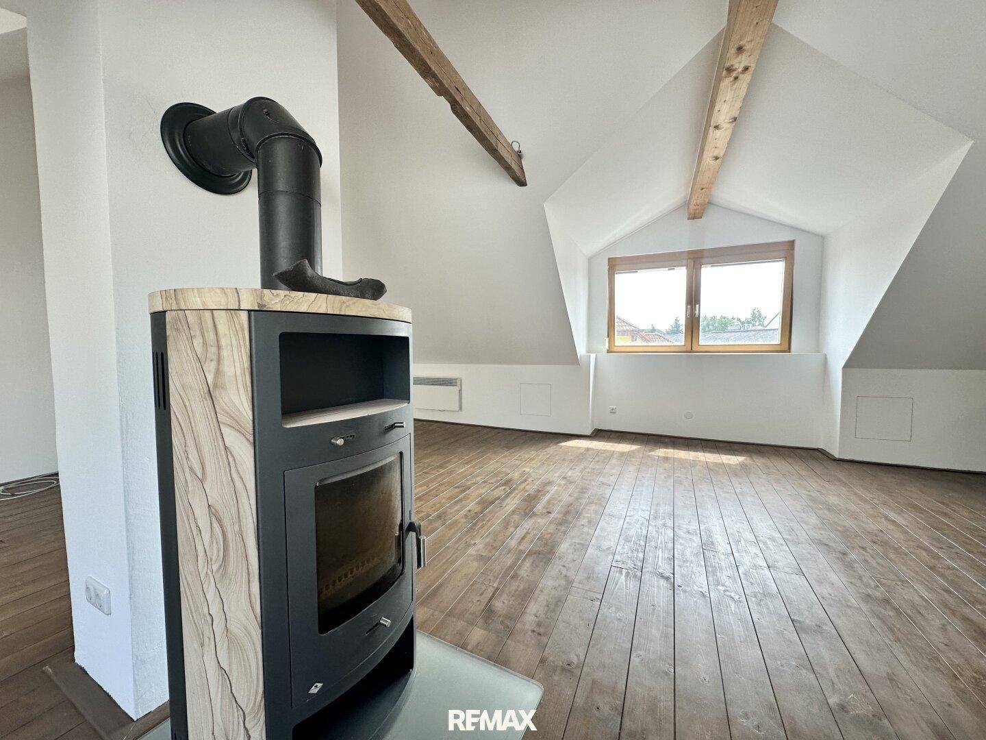 Heller Dachboden mit Holzdielenboden, schrägen Wänden und einem stilvollen Holzofen als Blickfang.