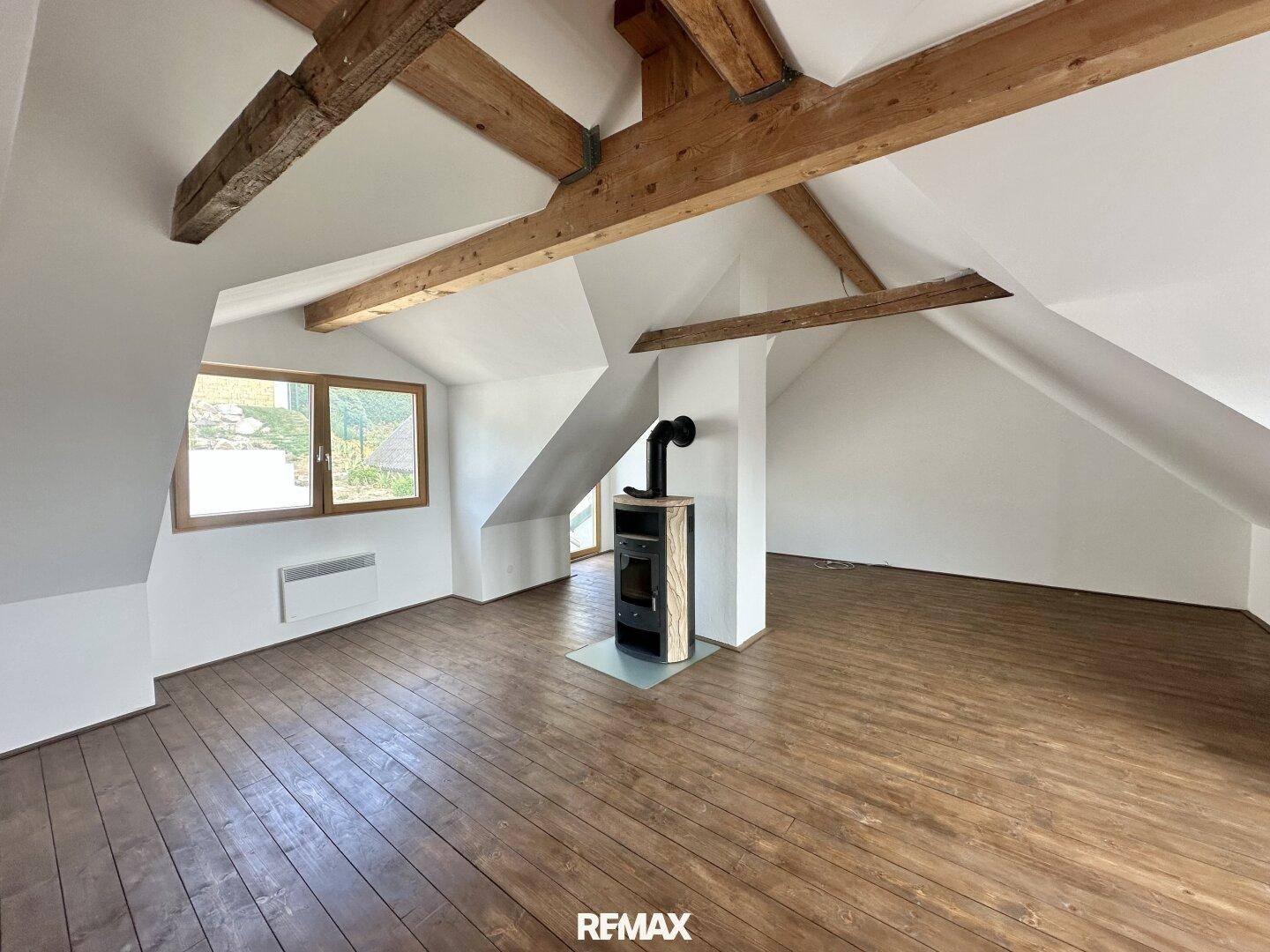 Geräumiger Dachboden mit Holzdielenboden, sichtbaren Holzbalken und einem modernen Holzofen.