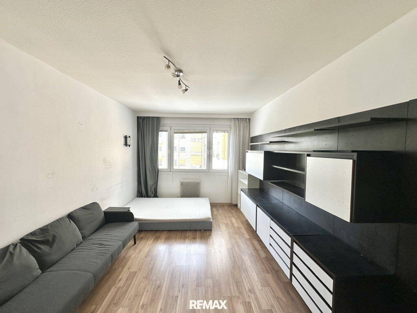Wohnzimmer mit Laminatboden und moderner Wandgestaltung, bietet Platz für ein Sofa und ein Bett.
