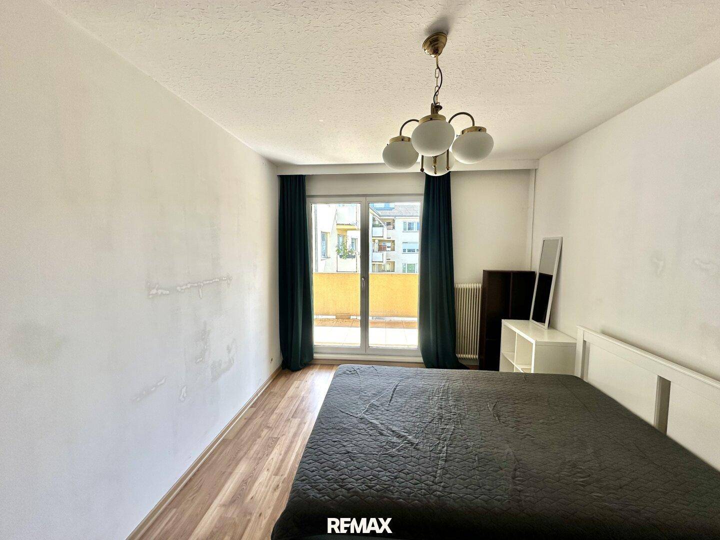 Helles Schlafzimmer mit Laminatboden und Balkonzugang, bietet eine einfache Einrichtung und viel Tageslicht.