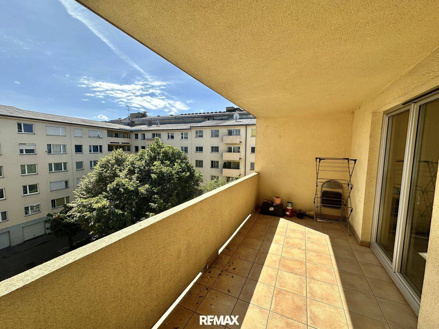 Heller Balkon mit Fliesenboden und grüner Aussicht auf den Innenhof, ideal für sonnige Stunden.