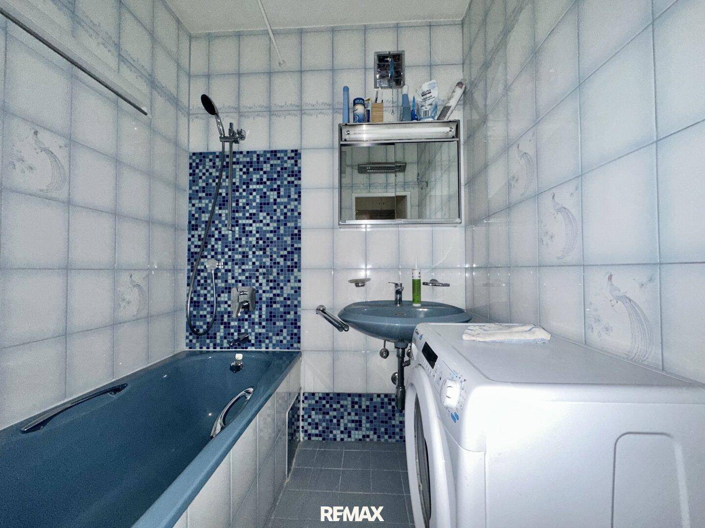 Badezimmer mit blauen Fliesen und Badewanne, ausgestattet mit Waschbecken und Waschmaschine.