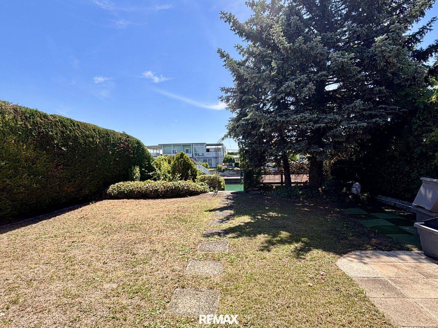 Trockener Gartenbereich mit Hecke und Bäumen, der einen Blick auf die umliegenden Häuser bietet.
