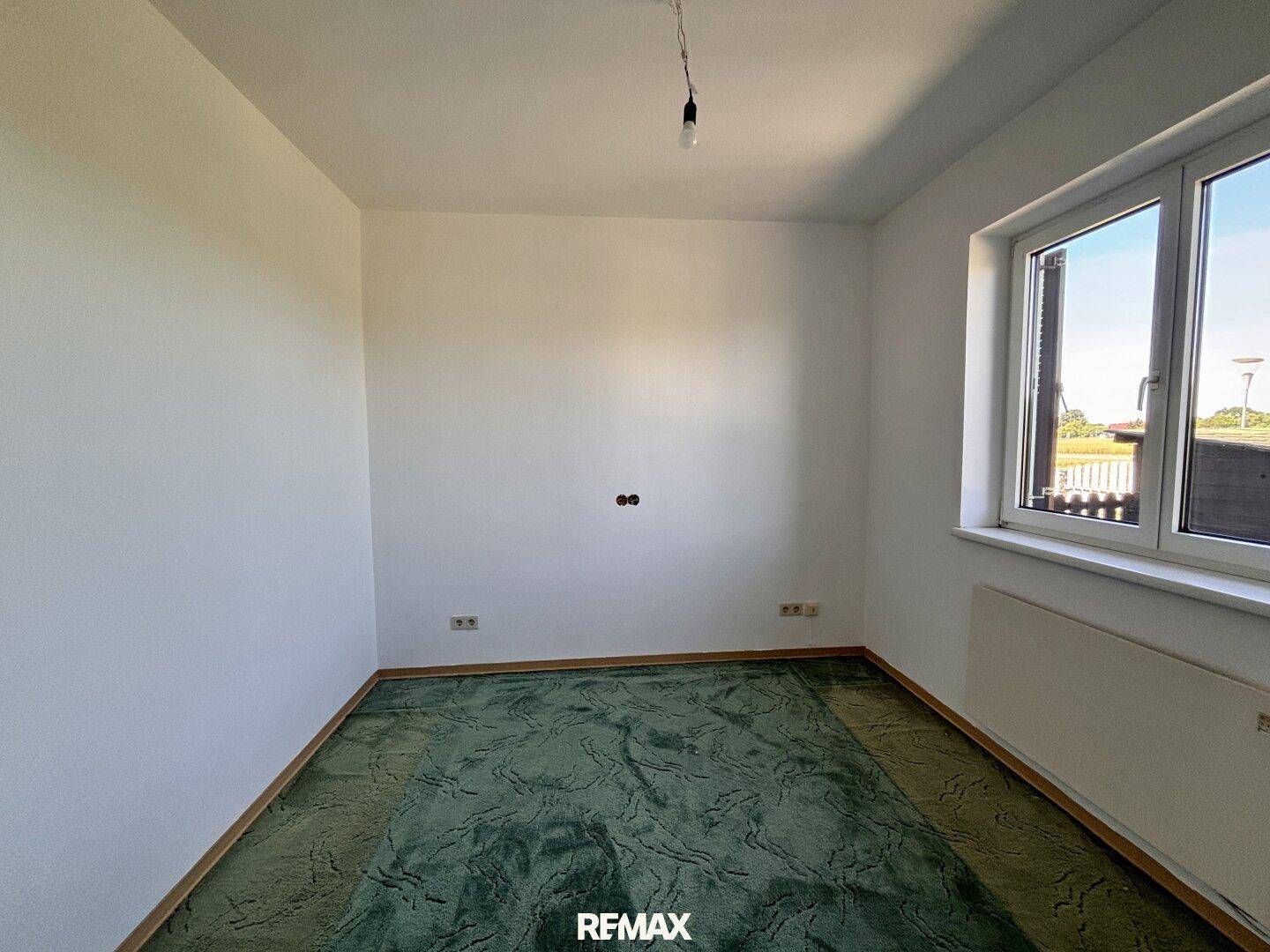 Schlafzimmer mit grünem Teppichboden und einem Fenster, das Tageslicht hereinlässt.