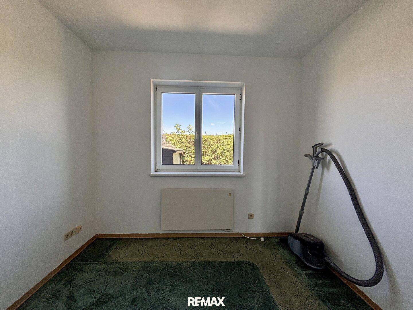 Helles Schlafzimmer mit grünem Teppichboden und einem Fenster mit Blick ins Grüne.