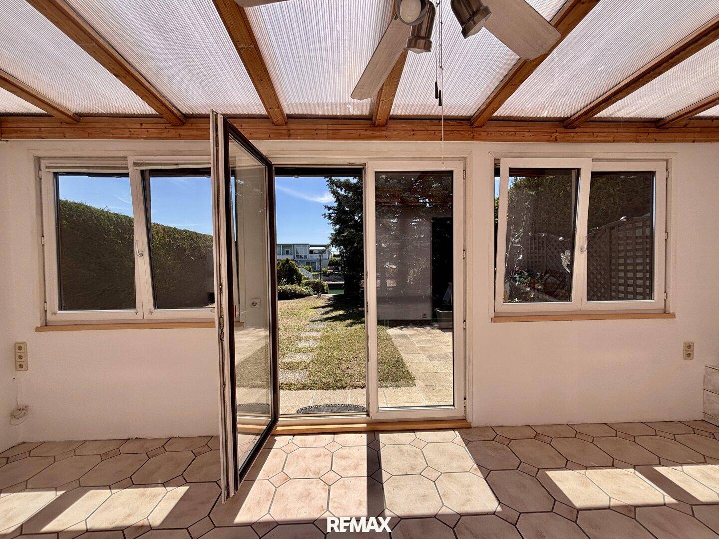 Heller Wintergarten mit Fliesenboden, Deckenventilator und direktem Zugang zum Garten.