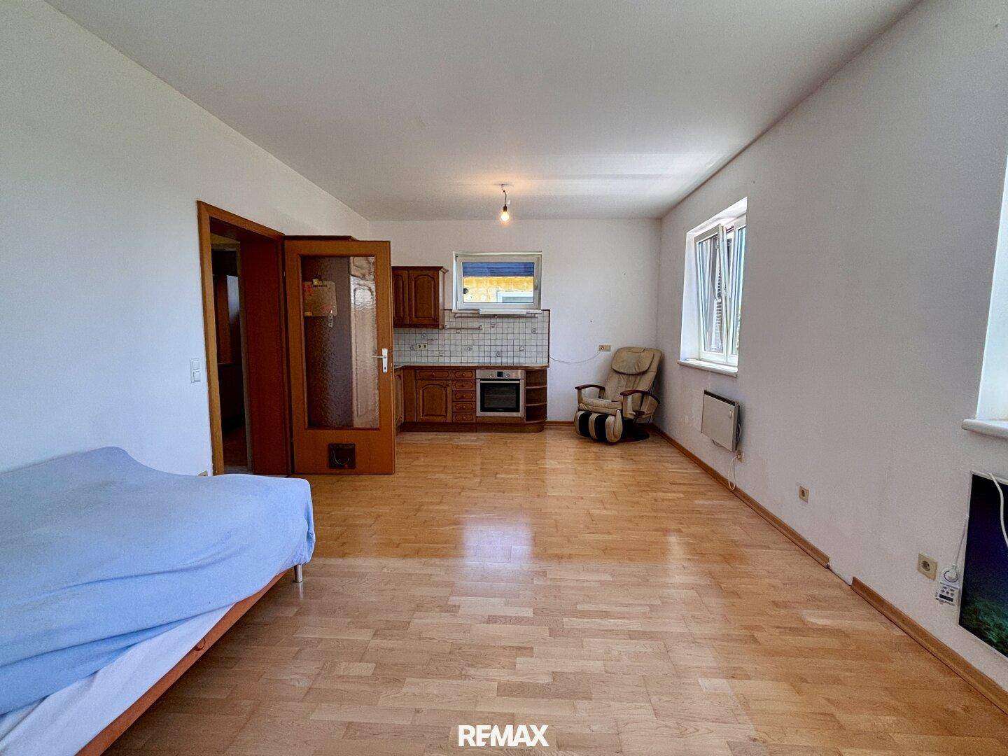Geräumiger Wohnbereich mit Parkettboden und einer kleinen Küchenzeile im Hintergrund.