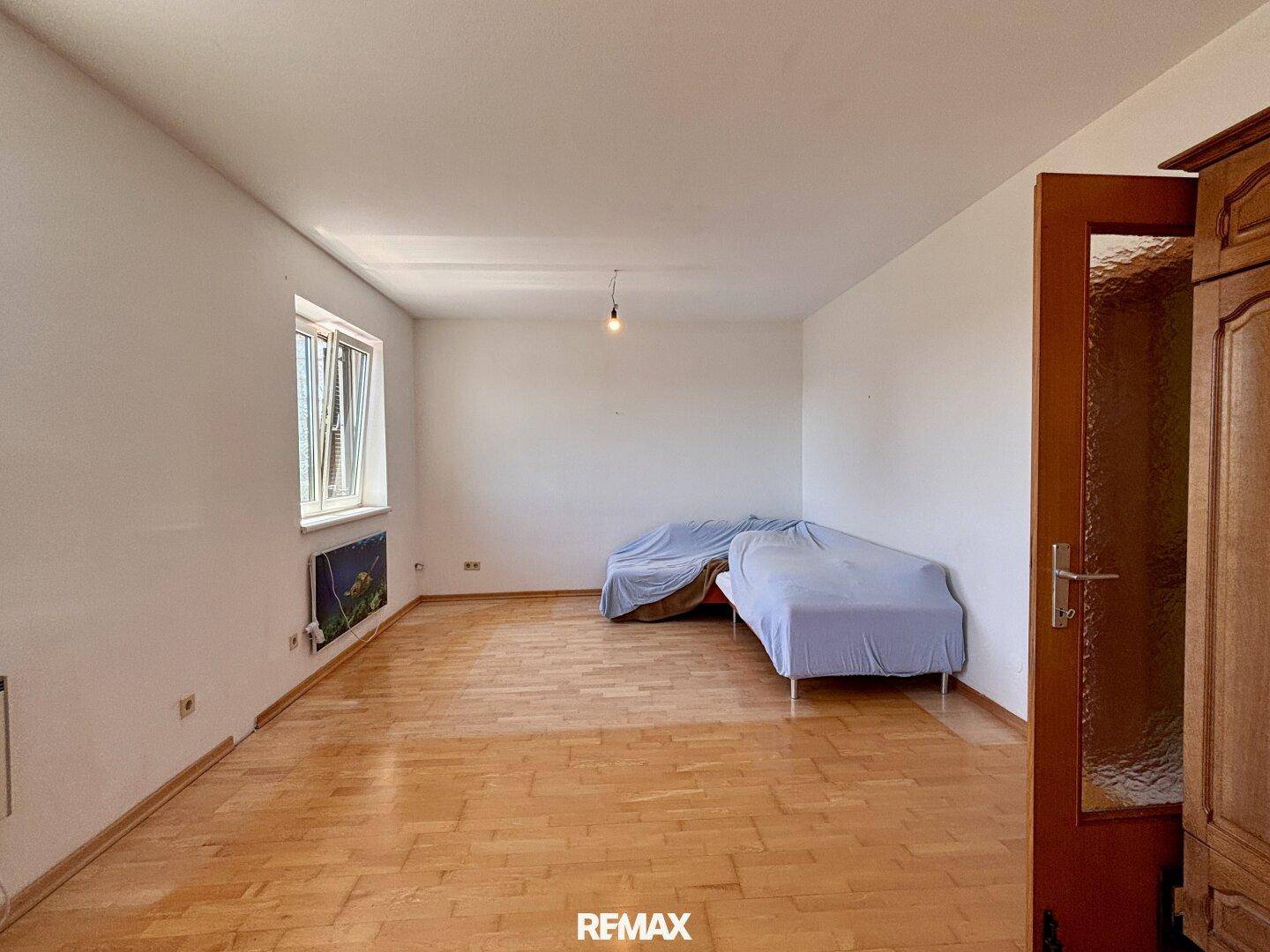 Heller Raum mit Parkettboden und einem Fenster, das den Blick nach draußen ermöglicht.