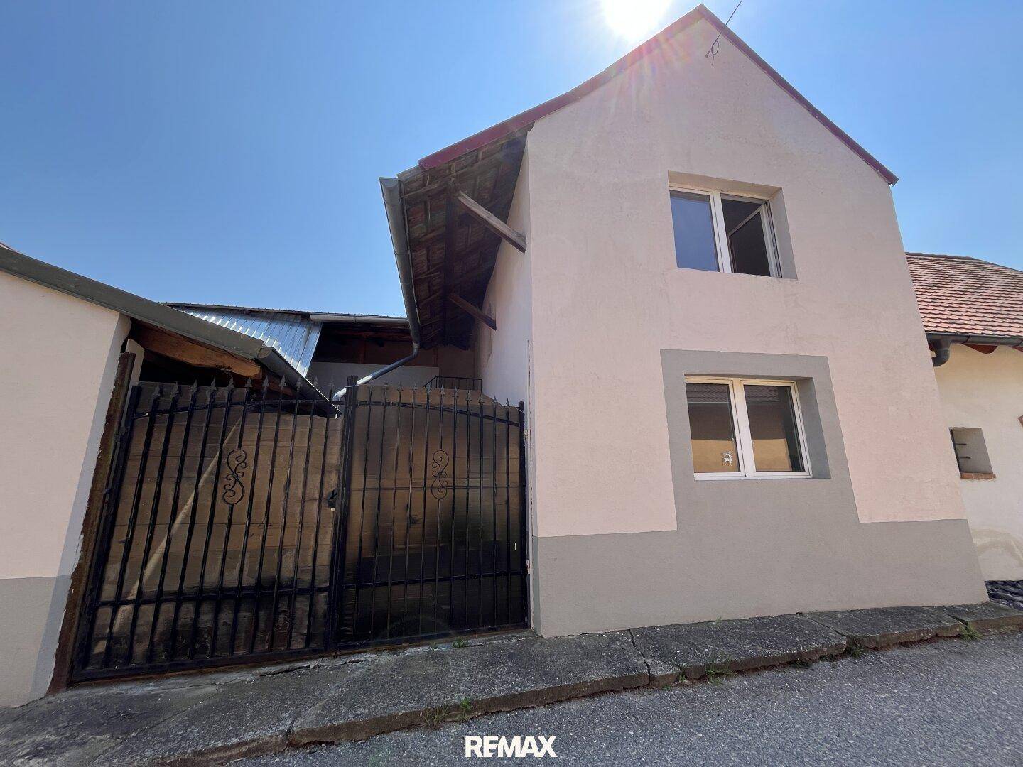 Fassade eines Hauses mit zwei Stockwerken, hellen Wänden und einem dunklen Tor.