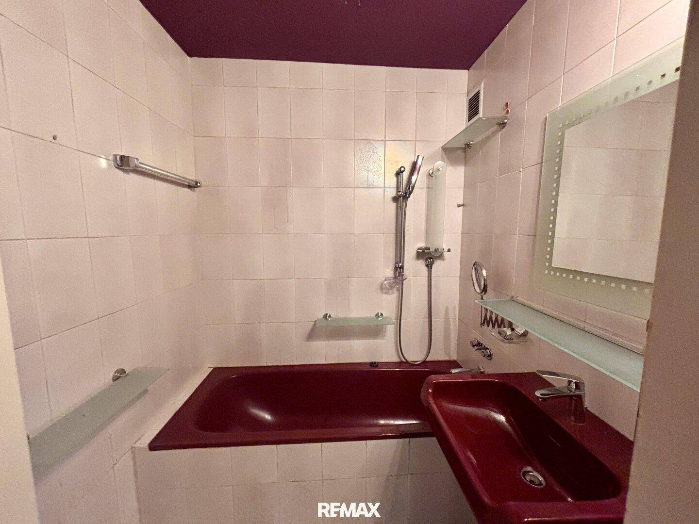 Badezimmer mit roten Sanitärobjekten, weißen Fliesen und einer auffälligen lila Decke.