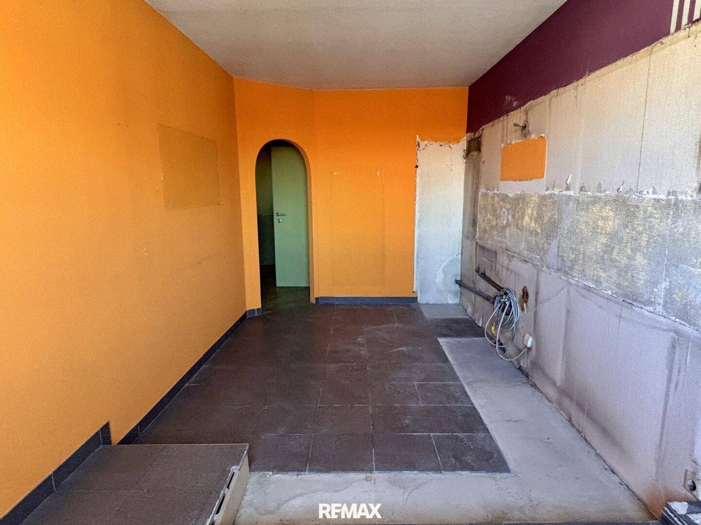 Renovierungsbedürftiger Raum mit orangefarbenen Wänden, Fliesenboden und einem Durchgangsbogen.