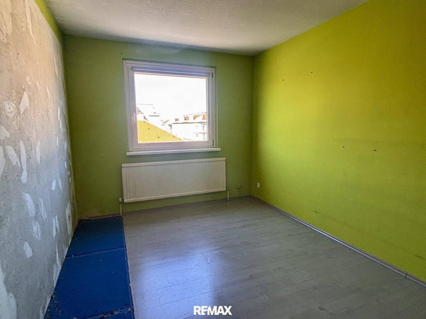 Helles Schlafzimmer mit grünen Wänden, Fenster und neu verlegtem Laminatboden.