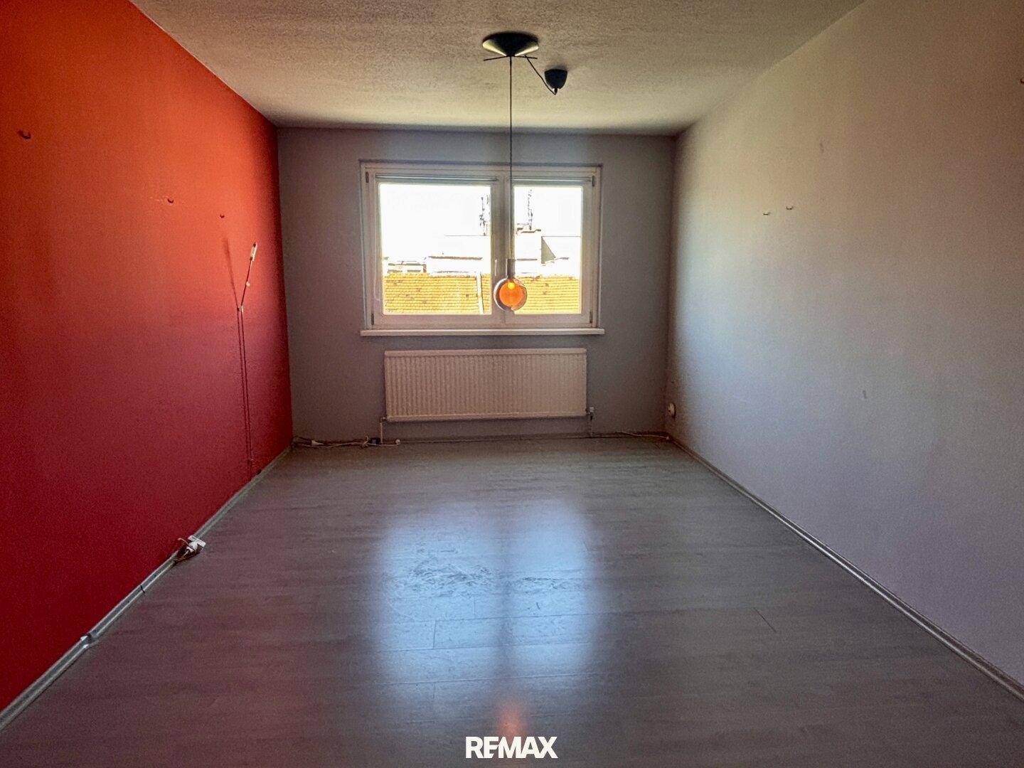 Heller Raum mit roten und grauen Wänden, Fenster und neu verlegtem Laminatboden.