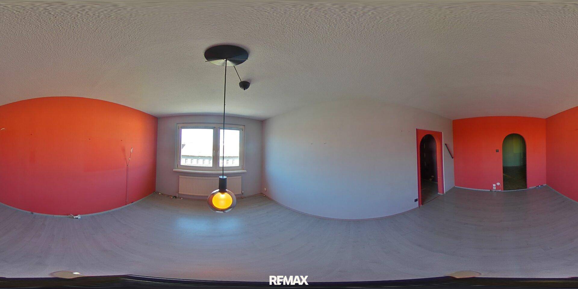 Unmöblierter Raum mit teilweise orangefarbenen Wänden, grauem Laminatboden und modernen Leuchten.