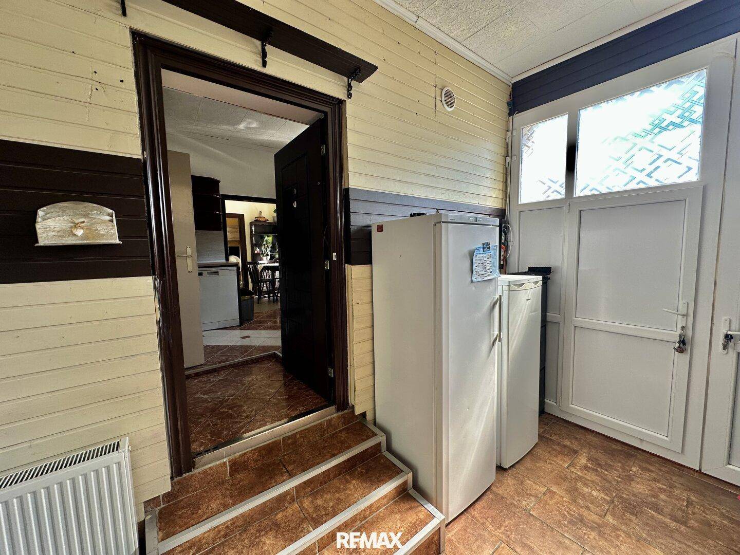 Überdachter Eingangsbereich mit zwei Kühlschränken und Zugang zum Innenbereich des Hauses.