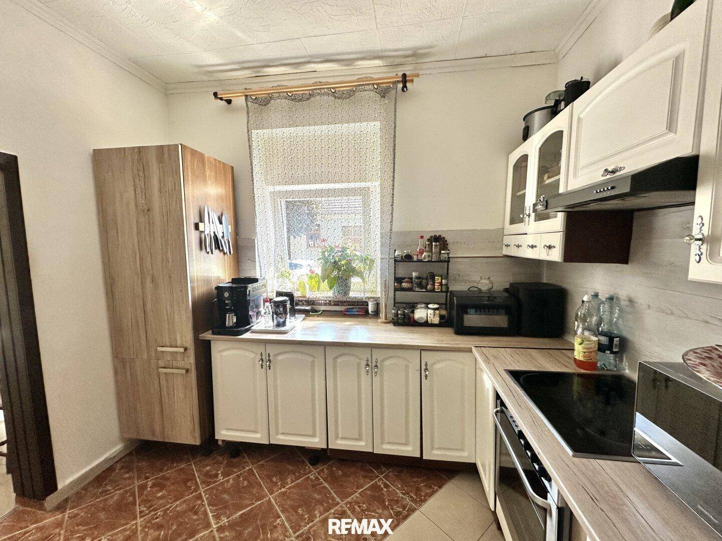 Funktionale Küche mit Induktionskochfeld, Backofen und weißen Schränken, mit Blick nach draußen.