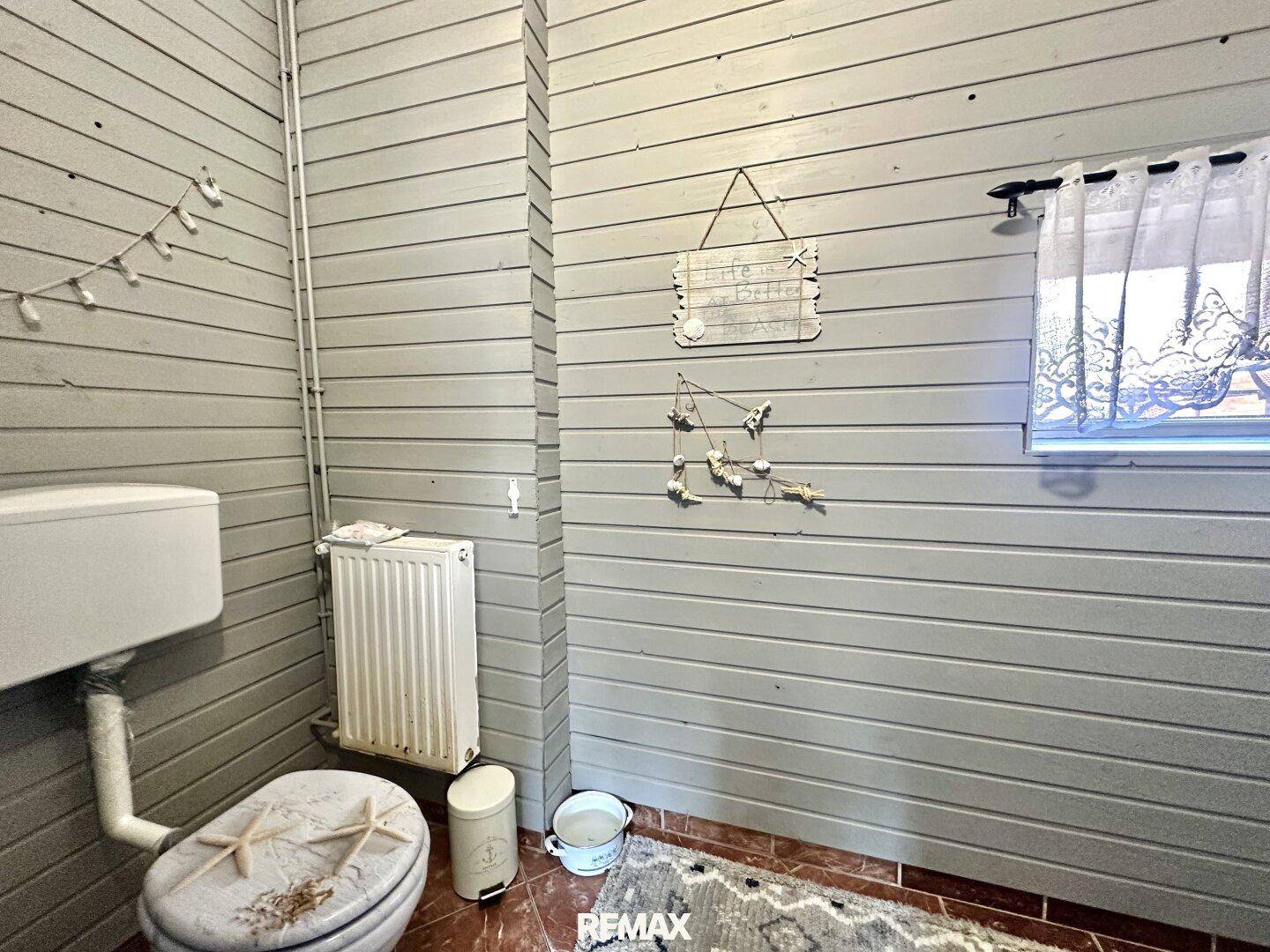 Kleines Gäste-WC mit Holzverkleidung an den Wänden und einem Fenster für Tageslicht.