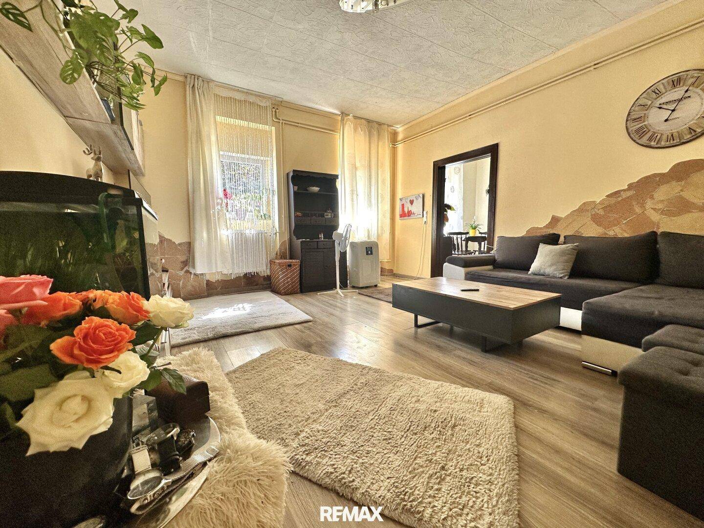 Helles Wohnzimmer mit Laminatboden, beigen Wänden und gemütlicher Sitzecke, gut beleuchtet.