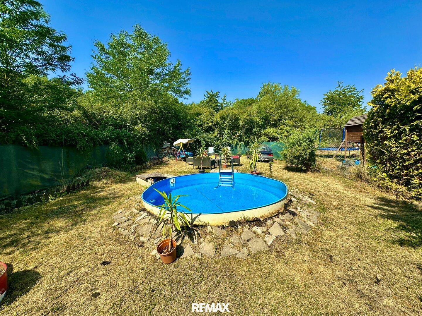 Sonniger Garten mit Aufstellpool, umgeben von üppigem Grün und Bäumen, ideal zum Entspannen.