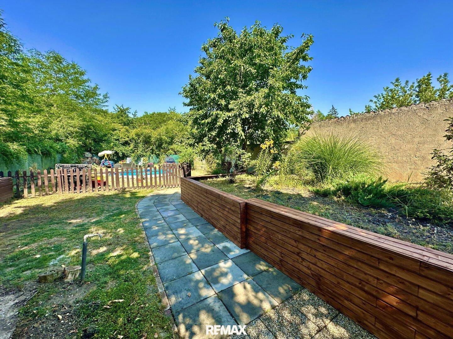 Gepflegter Gartenweg aus Steinplatten, umgeben von Rasen und Holzbeeten, führt durch die Anlage.