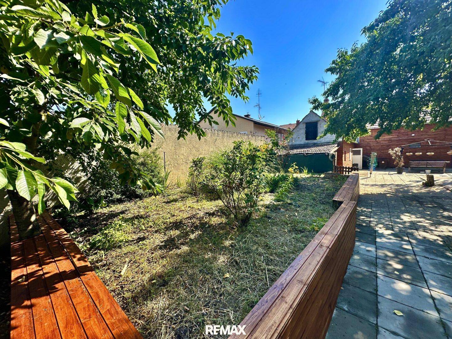 Offener Gartenbereich mit Rasenfläche und Holzbegrenzungen, umgeben von Bäumen und Sträuchern.
