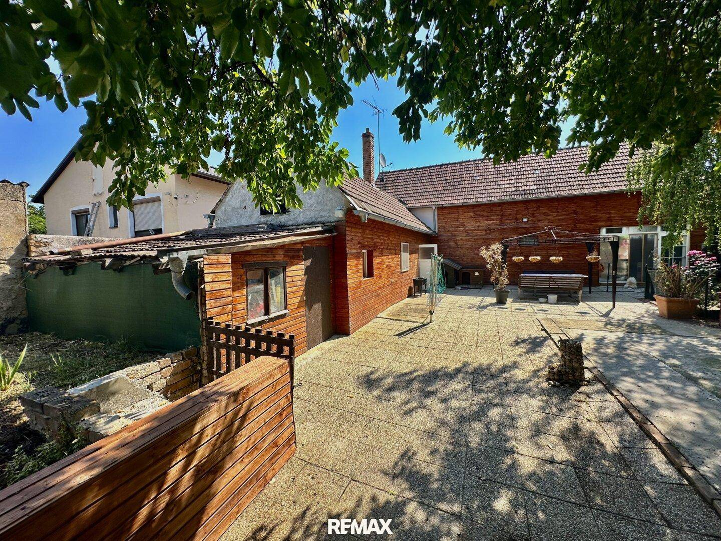 Großer gepflasterter Hinterhof mit Holzhaus und überdachtem Sitzbereich, ideal für Zusammenkünfte.