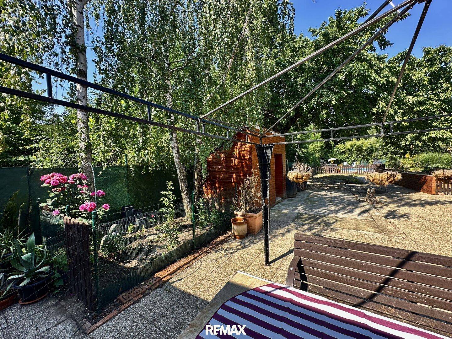 Grüner Gartenbereich mit Pergola, Sitzgelegenheiten und blühenden Pflanzen, ideal zum Entspannen.