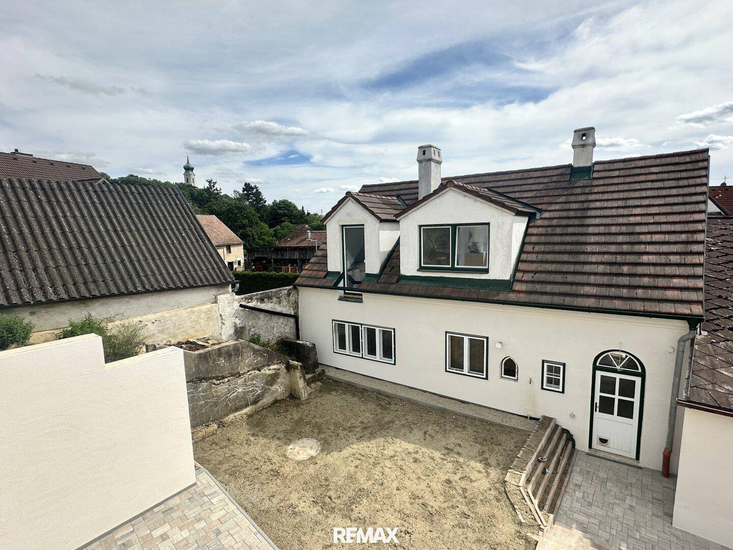 Rückansicht des Hauses mit einem leeren Innenhof, bereit für die Gestaltung, unter bewölktem Himmel.