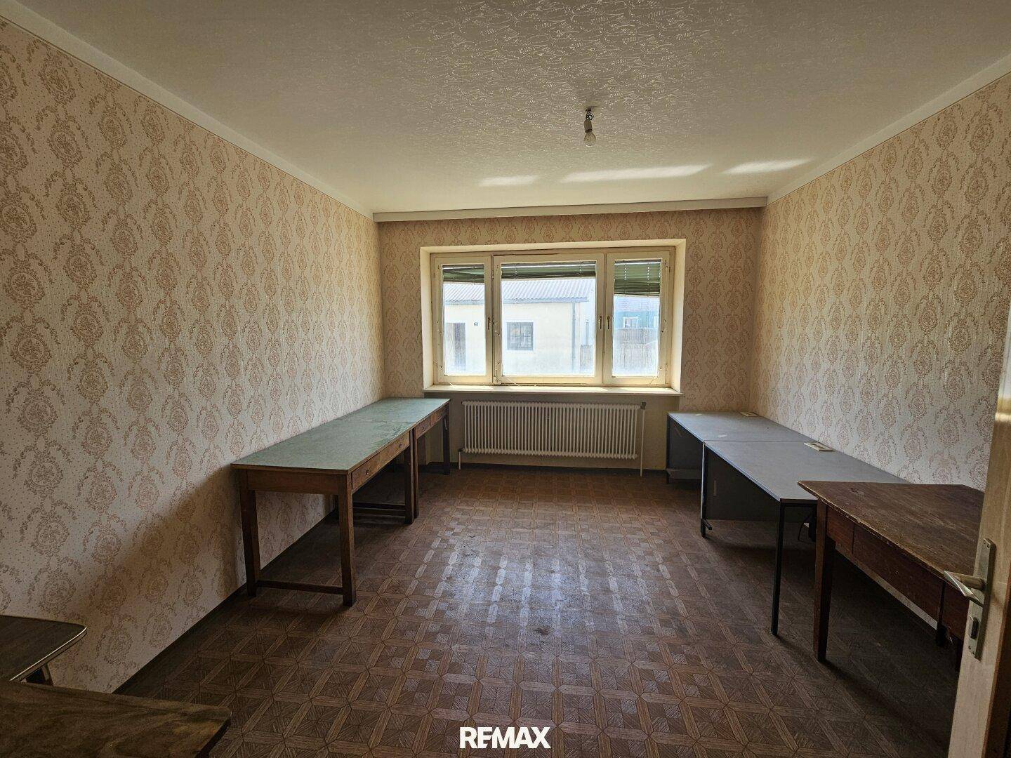 Helles Zimmer mit Parkettboden, gemusterter Tapete und Blick auf die Umgebung.