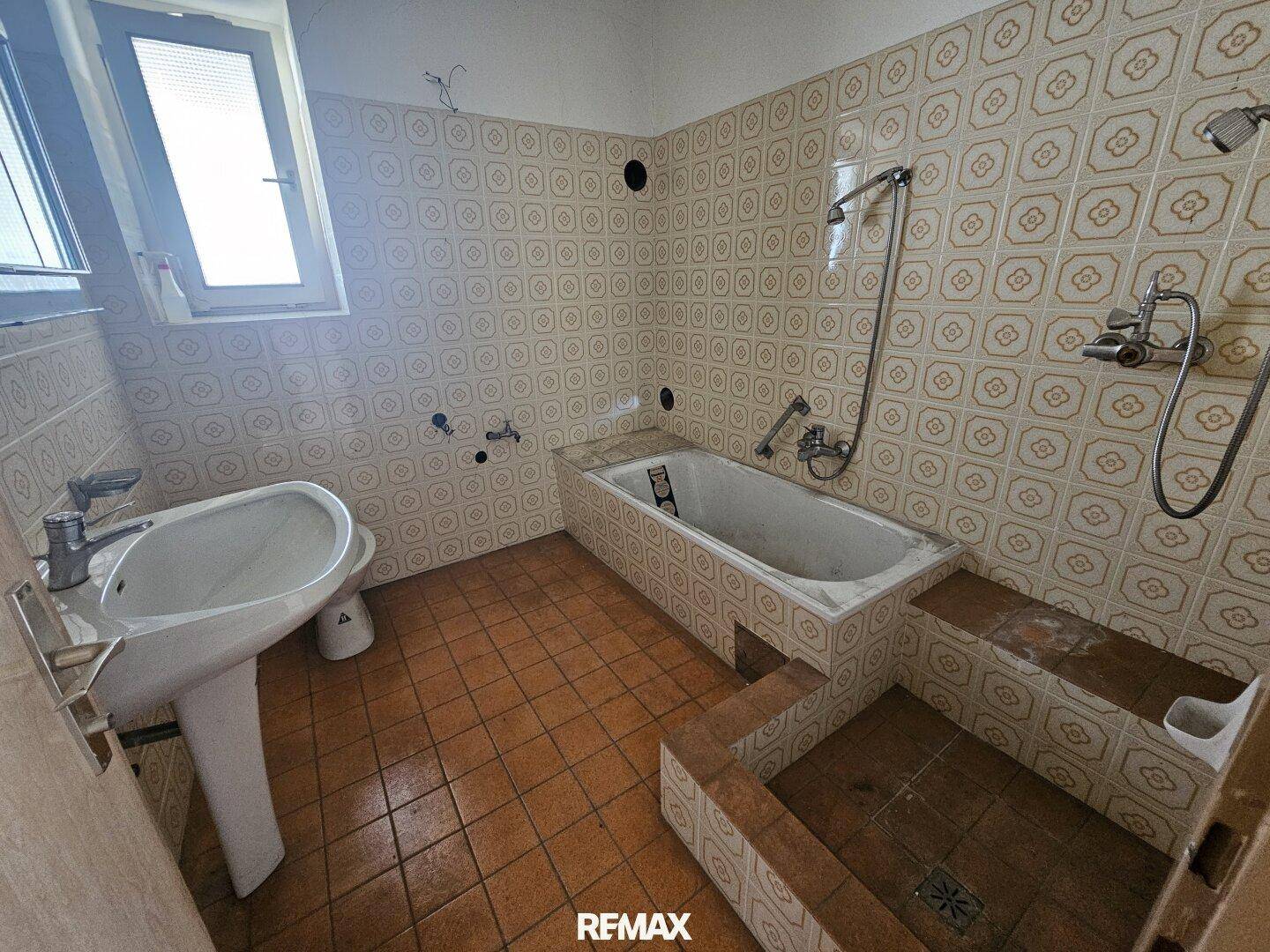 Badezimmer mit Badewanne, Waschbecken und gemusterten Fliesen im 80er-Jahre-Stil.