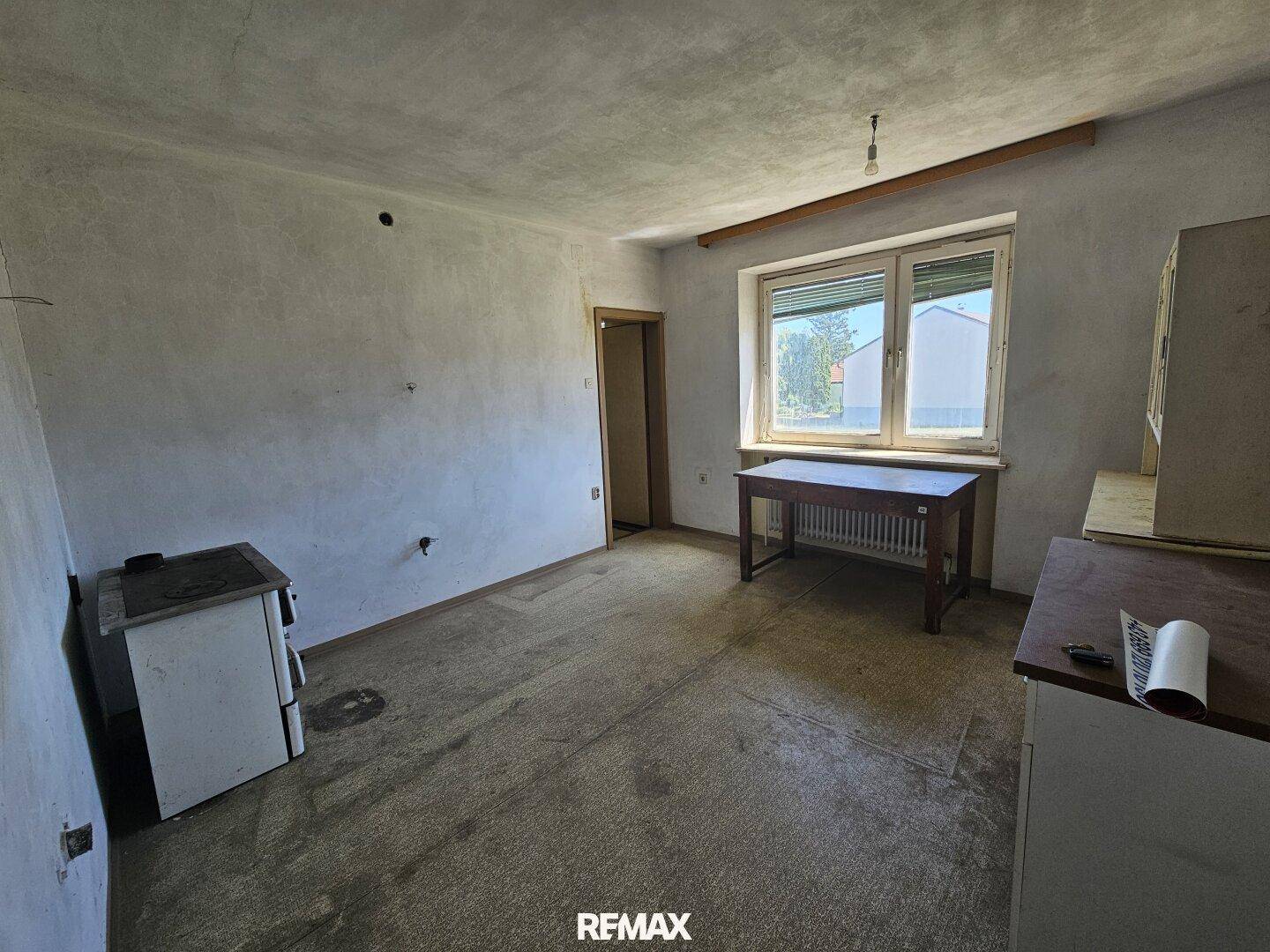 Einfache Küche mit altem Herd, Spüle und Fenster, bereit zur Renovierung.