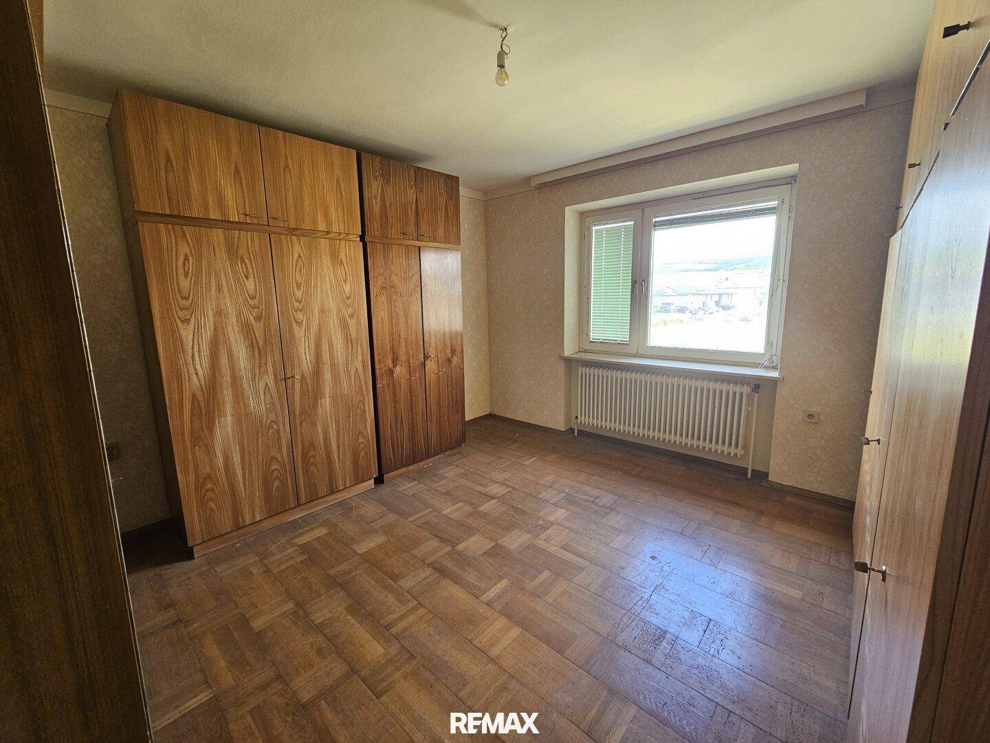 Schlafzimmer mit Parkettboden, Einbauschränken und Fenster mit Blick ins Grüne.