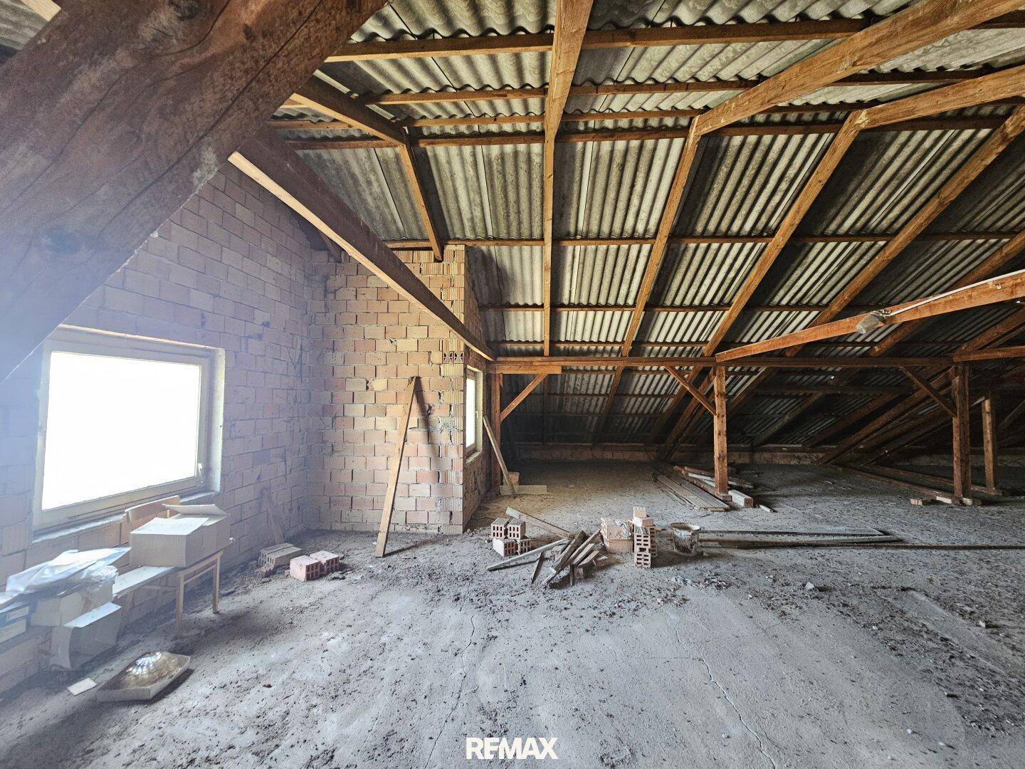 Geräumiger, unfertiger Dachboden mit sichtbaren Holzbalken und Ziegelwänden.