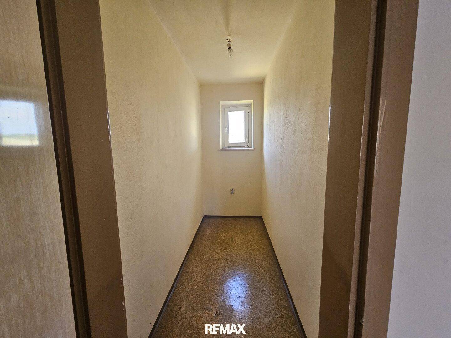 Schmaler Flur mit Fenster am Ende, der zu weiteren Räumen führt.