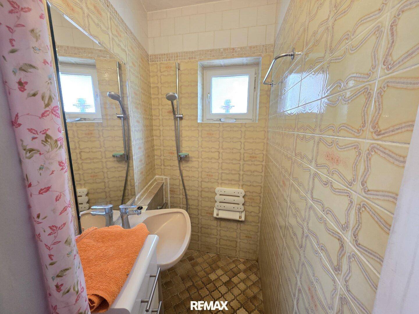 Kleines Badezimmer mit Dusche, Waschbecken und gemusterten Fliesen im Retro-Stil.