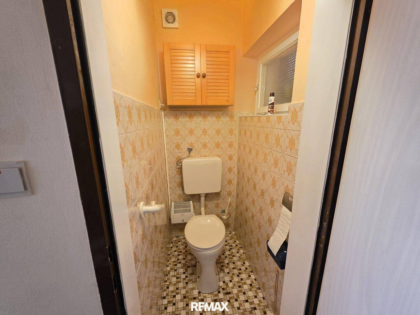 Separate Toilette mit WC und gemusterten Wandfliesen im Stil der 80er Jahre.