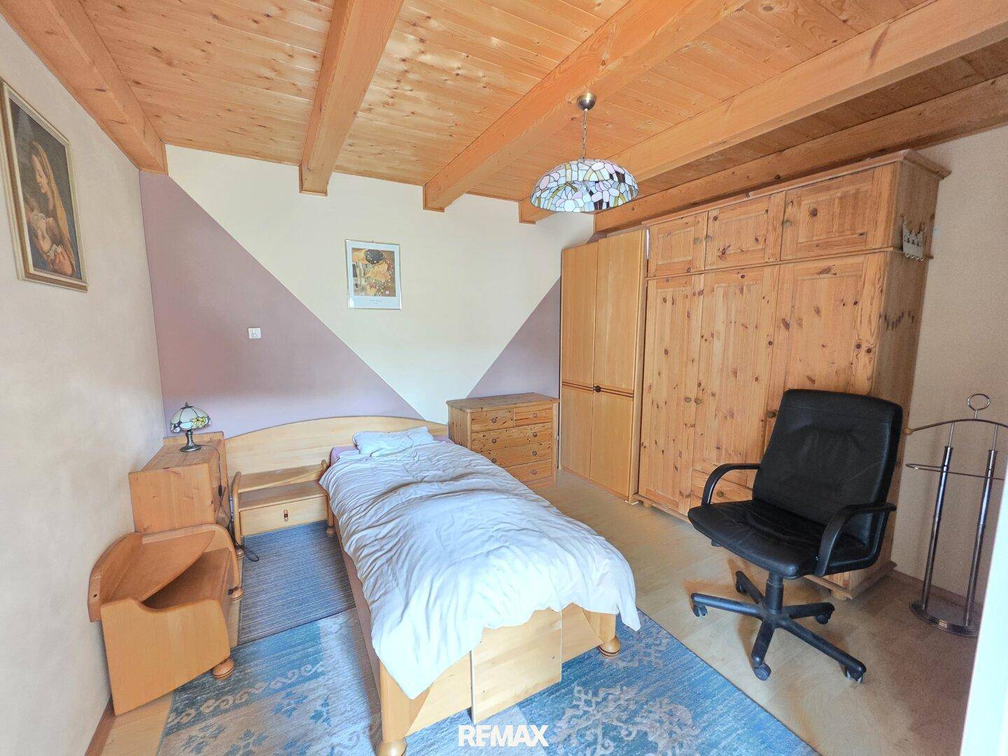 Schlafzimmer mit Holzbalkendecke, Holzmöbeln und schrägen Wänden, die Gemütlichkeit verleihen.