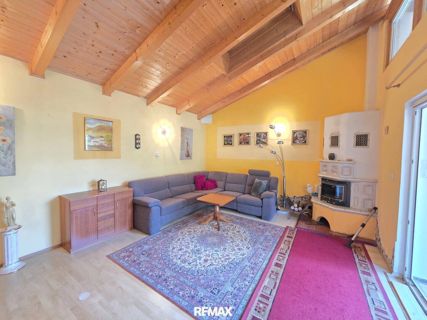 Geräumiges Wohnzimmer mit Holzbalkendecke, Kachelofen und einer gemütlichen Sitzecke.