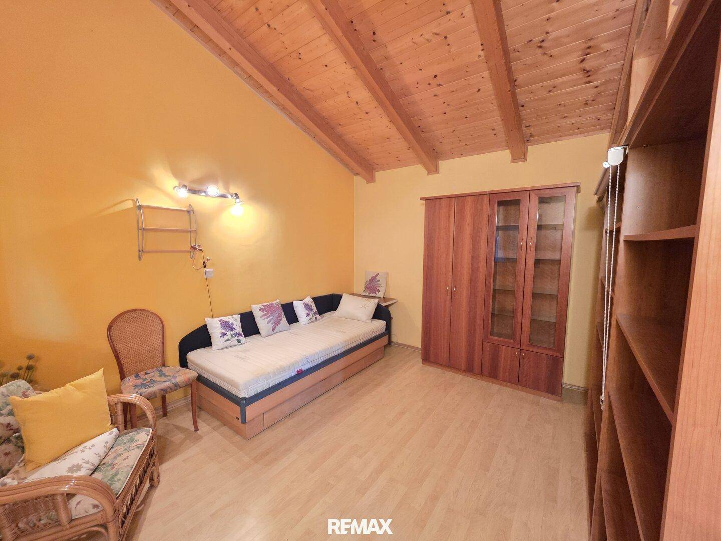 Helles Zimmer mit Holzbalkendecke, Holzschrank und einem Schlafsofa, ideal als Gästezimmer.