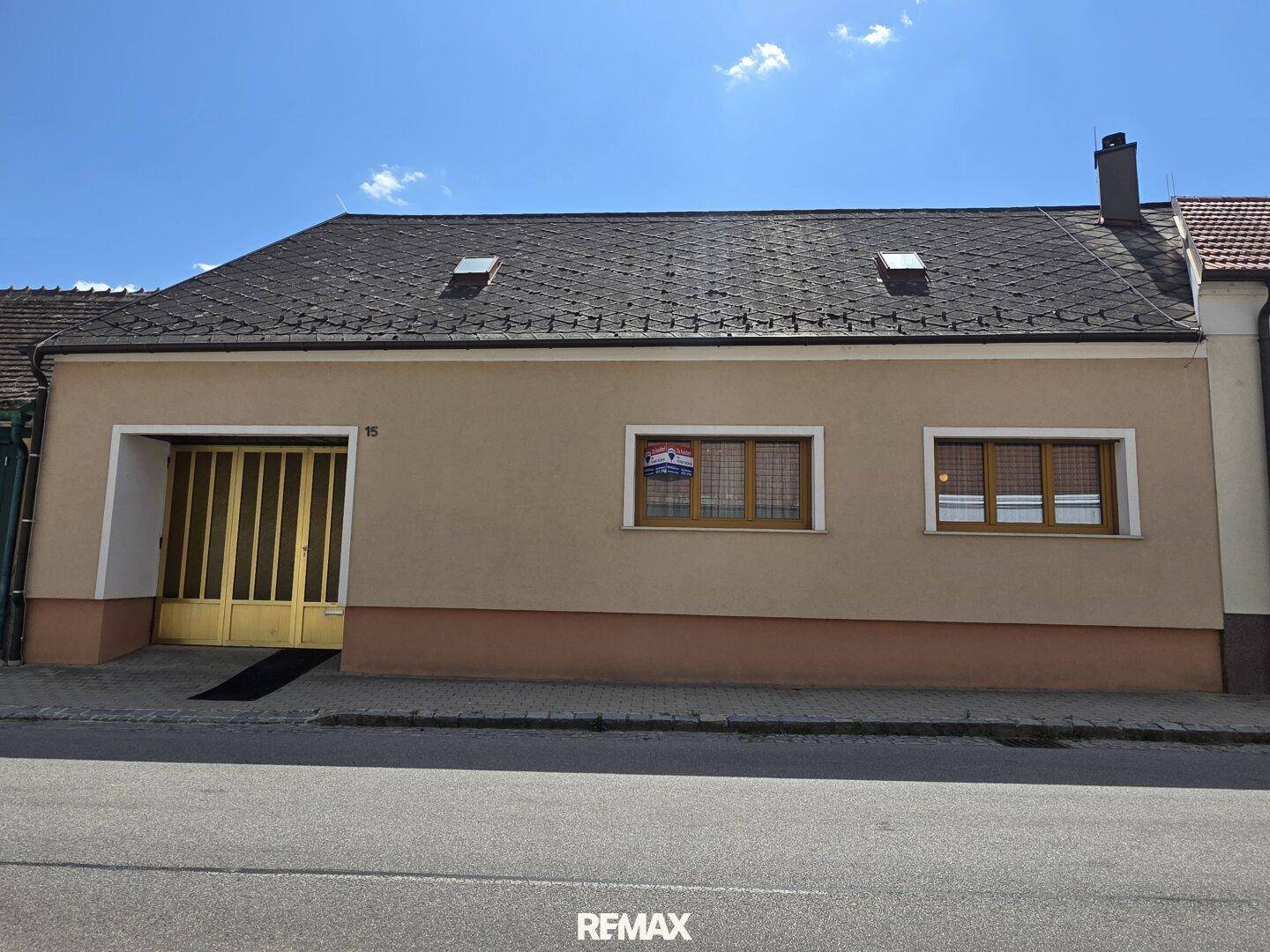 Fassade eines Einfamilienhauses mit Satteldach und gelbem Garagentor an der Straße.