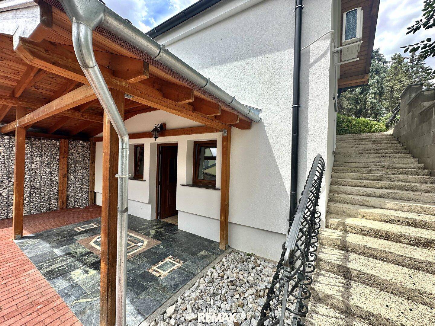 Seitenansicht des Hauses mit überdachtem Eingangsbereich und Außentreppe.