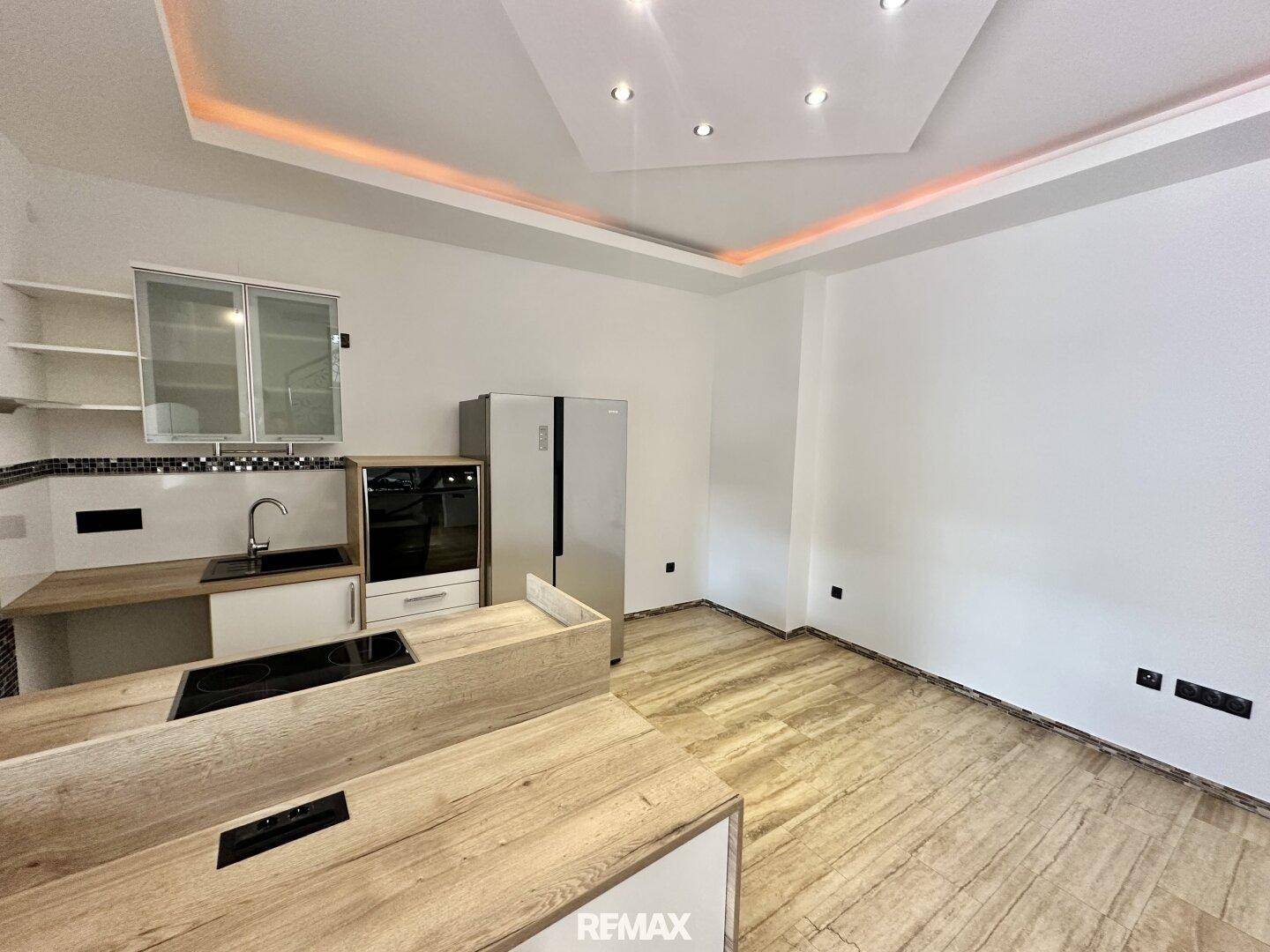 Moderne Küche mit Holzoptik-Arbeitsplatten, Einbaugeräten und indirekter Deckenbeleuchtung.